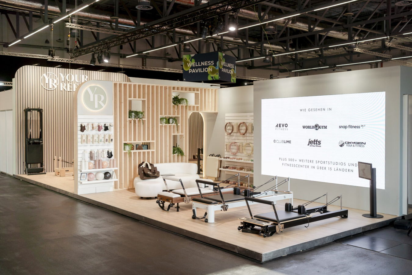 Messestand für Pilates- und Wellnessgeräte mit Trainingsgeräten und Markenwand