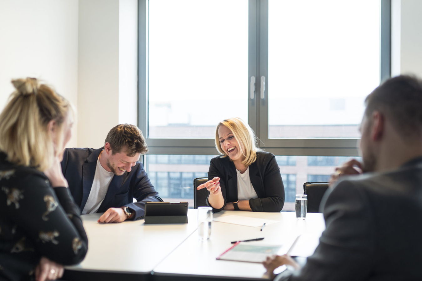 Vier Personen sitzen in einem Besprechungsraum und lachen während eines Meetings